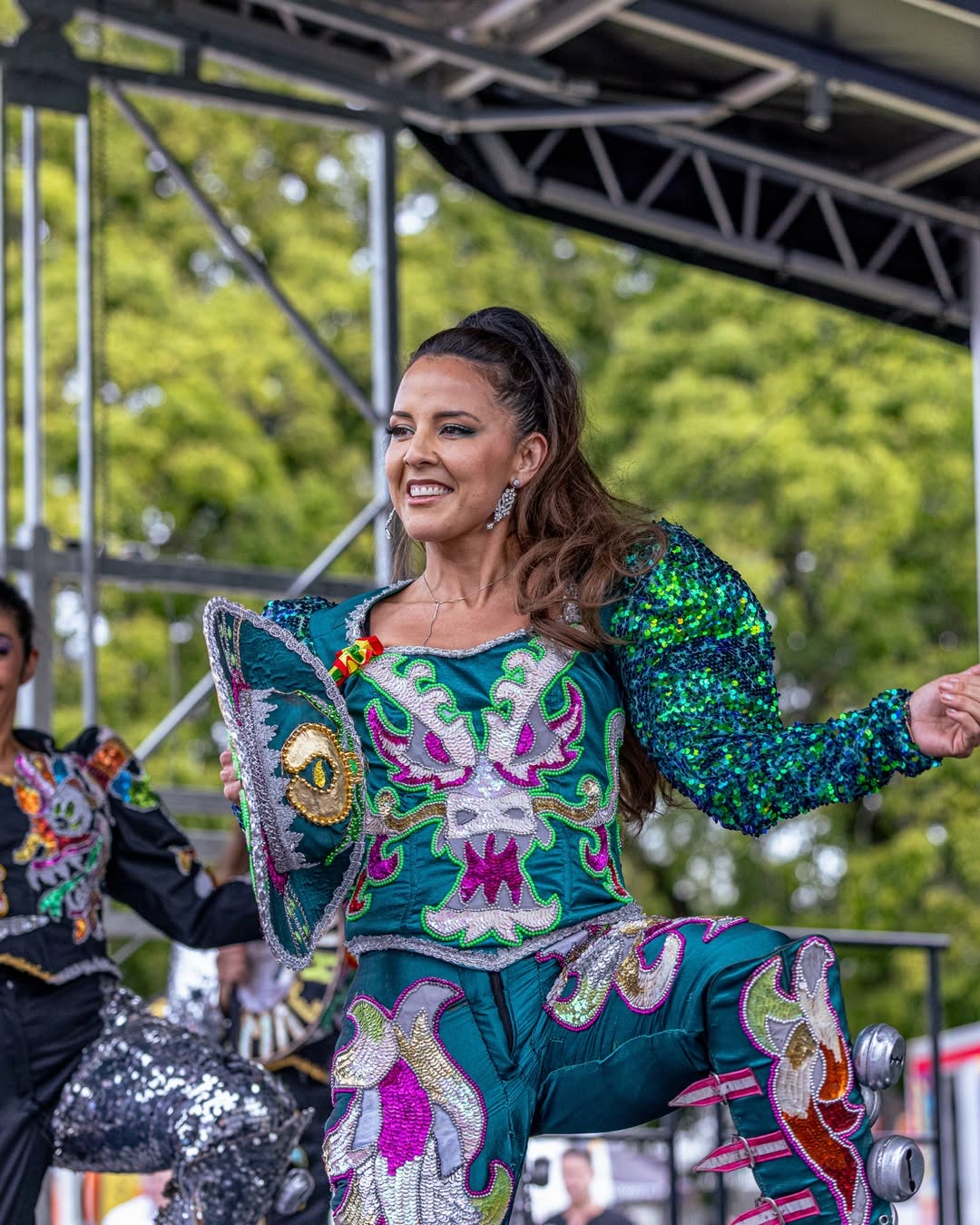 A caporales dancer in a sequined costume performing on stage at Lazos Latinos